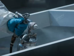 Une personne en manteau blanc pulvérise une surface métallique.