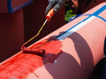 Gros plan de la main d'une personne utilisant un pinceau pour appliquer de l'apprêt blanc sur une surface en bois, la préparant pour la couche de peinture finale.