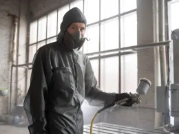 Un homme masqué en tenue de protection pulvérise de la peinture.