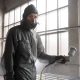 Un homme masqué en tenue de protection pulvérise de la peinture.